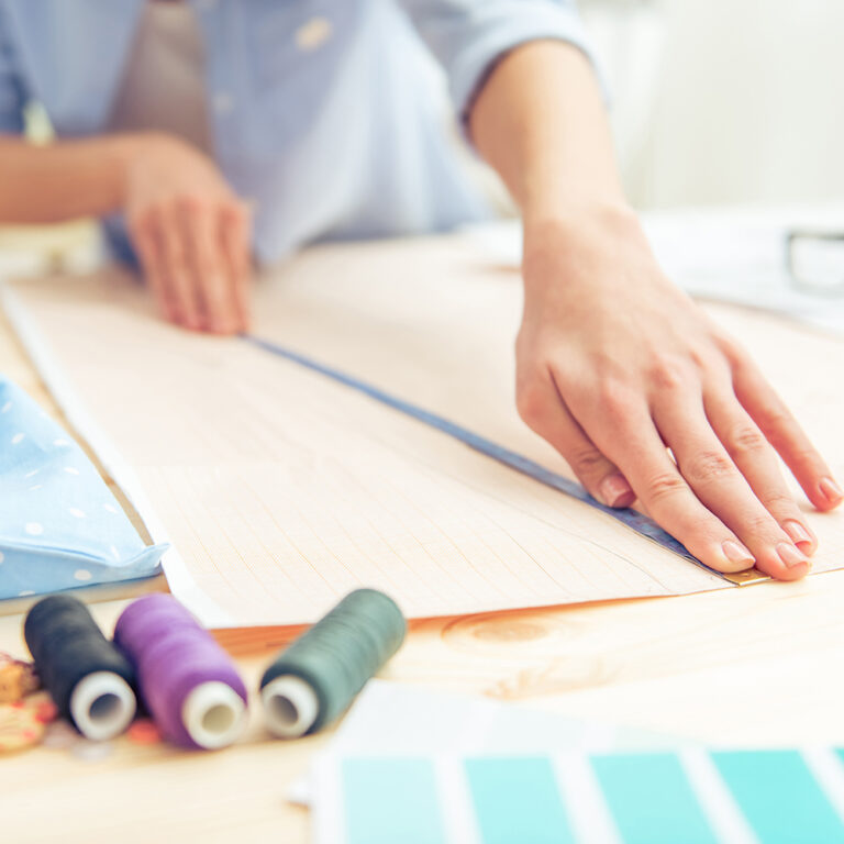 Cropped image of beautiful young designer working with sketches and measure tape in dressmaking salon